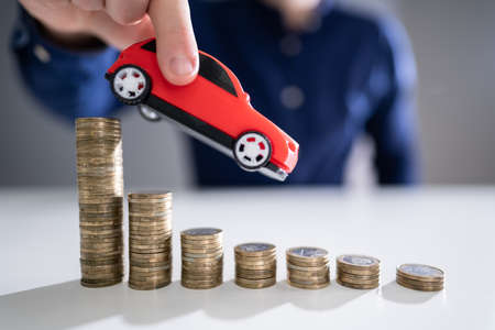 Close-up Of A Person's Hand Flying Car Over Declining Stacked Coins