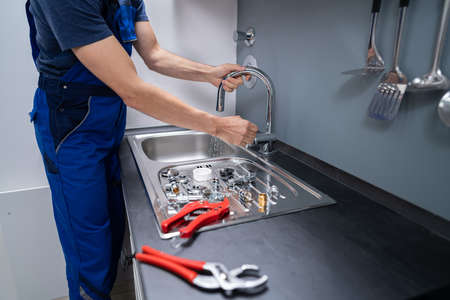 Happy Young Male Plumber Fixing Faucet In Kitchen