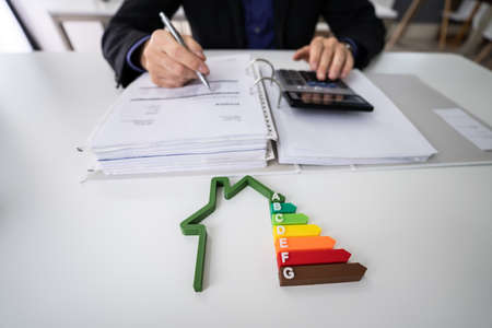 Close-up Of A Businessman Using Calculator Holding Outline Of House Model With Energy Efficiency Rateの写真素材