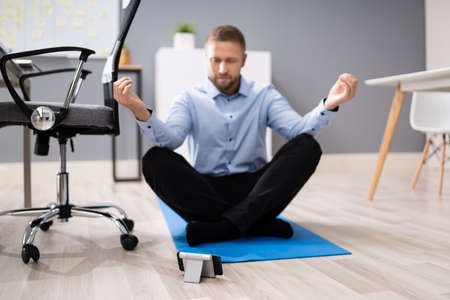 Businessman Meditating Using Smartphone App In Officeの写真素材