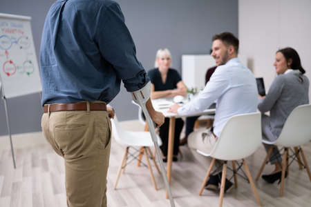 Handicapped Businessman Walking On Hardwood Floor With Crutches At Workplace