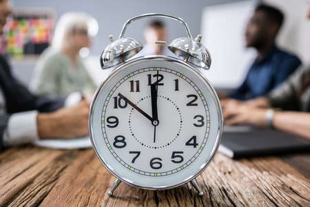 Close-up Of Alarm Clock In Front Of Businesspeople Working In Office