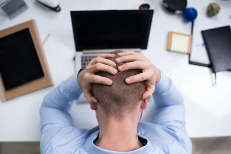 High Angle View Of Young Stressed Businessman In Front Of Laptop At Desk