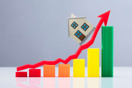 An Increasing Business Graph And Red Arrow Sign With House Model Over Reflective Deskの写真素材