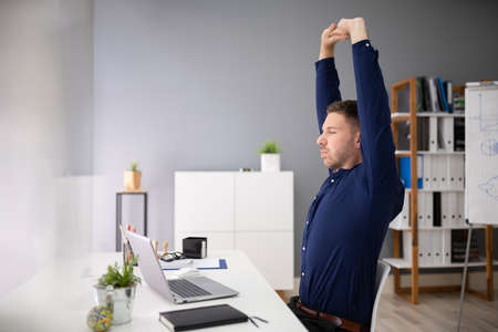 Young Businessman Stretching At Workplace In Office