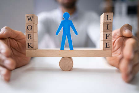 Human Figure Standing Between Work And Life Wooden Blocks On Seesaw Being Protected By Businesspersonの写真素材