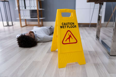 Mature Man Falling On Wet Floor In Front Of Caution Sign At Office