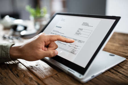 Close-up Of A Businessperson's Hand Analyzing Invoice On Laptop At Workplaceの写真素材