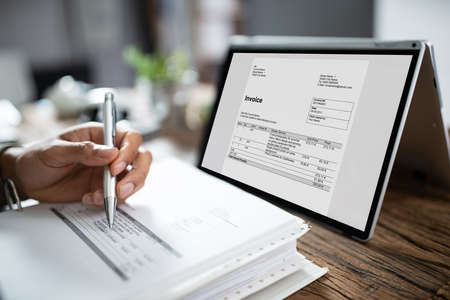 Close-up Of Businessman's Hands Working On Invoice On Laptop At Officeの写真素材