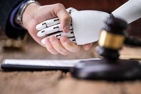 Robot Shaking Hands With Judge Near Gavel On Wooden Desk