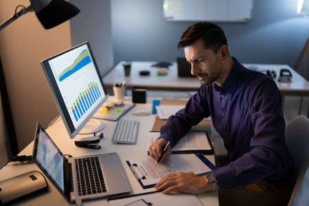 Mid Adult Businessman Working Late At Desk In Officeの写真素材