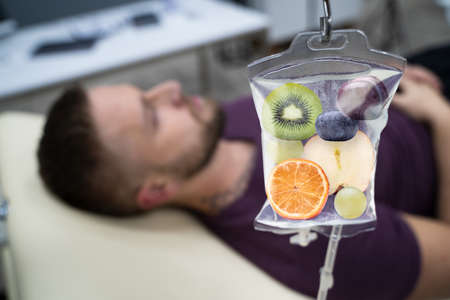 Man In In Hospital Getting IV Infusion Of Fruit Slices Inside Saline Bagの写真素材