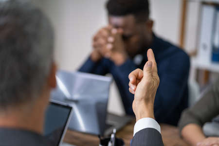 Close-up Of Businessperson Quarreling To Young Colleague At Desk