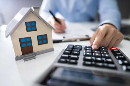 Close-up Of A Person Hand Calculating A Real Estate Property Tax On Wooden Desk