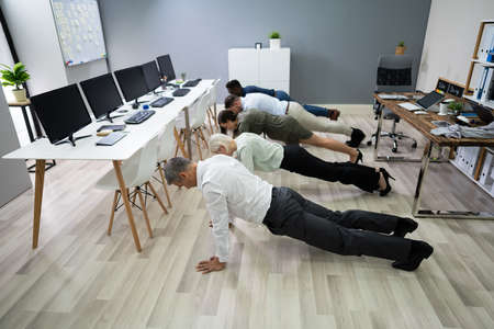 Group Of People Doing Pushups Exercise At Workplaceの写真素材