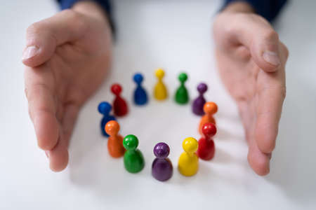 Close-up Of A Person's Hand Protecting Multicolored Pawns Forming Circle Over White Desk