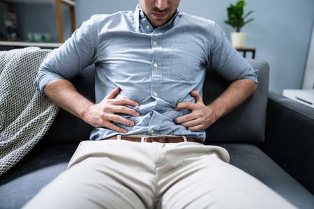 Man With Stomach Ache Sitting On Couch At Homeの写真素材