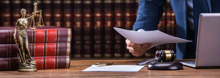 Midsection Of Lawyer Holding Documents Near Mallet And Laptop At Desk In Courtroom