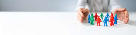 Close-up Of A Person's Hand Protecting Multicolored Pawns Forming Circle Over White Desk