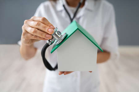 Close-up Of A Doctor's Hand Holding Stethoscope On House Modelの写真素材