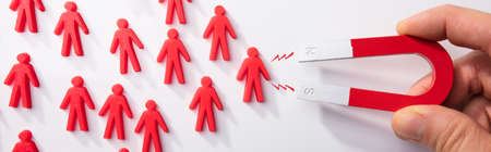 Close-up Of A Human Hand Attracting Human Figures With Magnet On White Background