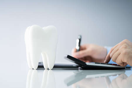 Close-up Of Tooth In Front Of Businessperson Calculating Billの写真素材
