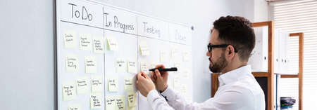 Businessman Writing On Sticky Notes Attached To White Board In Office