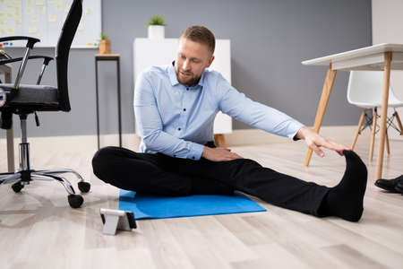 Businessman Doing Stretching Workout Using Smartphone App In Office