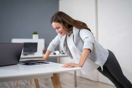 Side View Of A Young Businesswoman Doing Push Up On Office Desk
