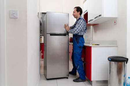 Young Male Mover Placing Steel Refrigerator In Kitchenの写真素材