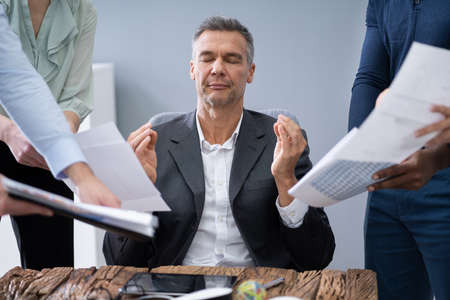 Mature Businessman Meditating While Surrounded By His Executivesの写真素材
