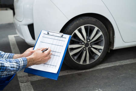 Young Mechanic Writing On Clipboard White Examining Car Wheel