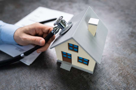 Close-up Of A Person Hand Holding Stethoscope On House Model At Wooden Deskの写真素材