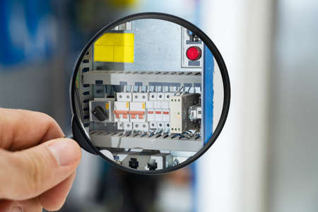 Male Technician Examining Fusebox With Magnifying Glass