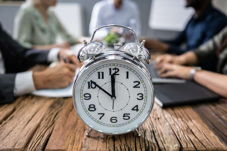 Close-up Of Alarm Clock In Front Of Businesspeople Working In Officeの写真素材