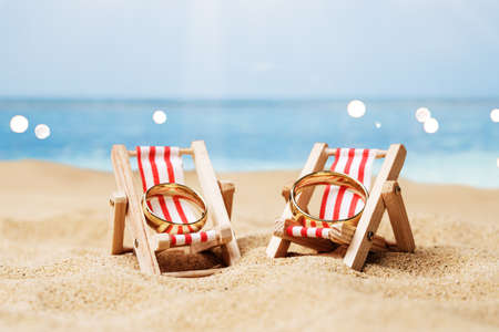 Golden And Shiny Wedding Rings On Deck Chairs On Sand At Beachの写真素材