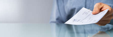 Close-up Of A Human Hand Giving Cheque On Desk