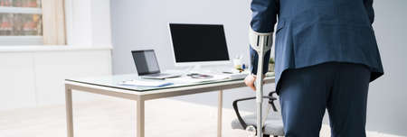 Handicapped Businessman Walking On Hardwood Floor With Crutches At Workplaceの写真素材