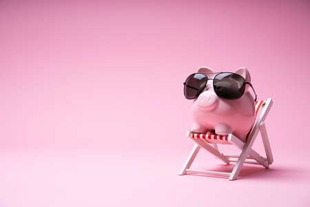 Pink Piggy Bank With Sunglasses On The Small Deck Chair On Pink Backgroundの写真素材