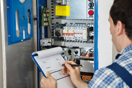 Cropped Image Of Male Electrician Holding Clipboard While Examining Fusebox