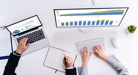 Two Businesspeople Examining Graph On Computer At Workplace