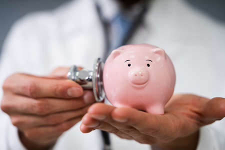 Midsection Of Male Doctor Examining Piggybank With Stethoscope Over White Backgroundの写真素材