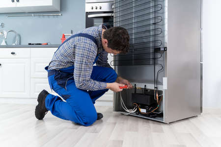 Male Worker Repairing Refrigerator With Screwdriver In Houseの写真素材