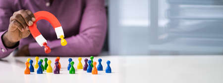 Hand Holding Red Horseshoe Magnet Attracting Pawn Figuresの写真素材