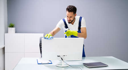 Portrait Of Happy Male Janitor Cleaning Computer On Office Deskの写真素材