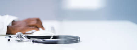 View Of Stethoscope With Doctor Using Computer Keyboard In Clinic