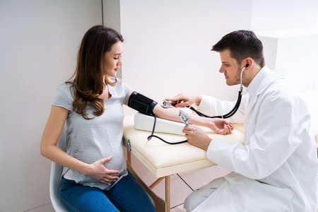 Doctor Measuring Blood Pressure Of Pregnant Woman In Clinic