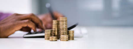 Close-up Of A Businessman Calculating Financial Report With Stack Of Coins On Desk In Office