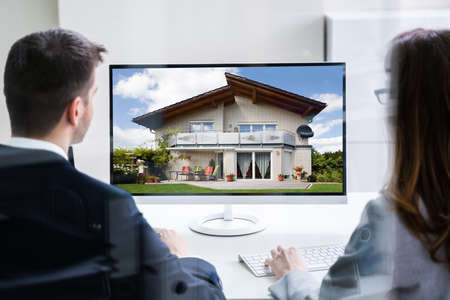 Two Businesspeople Looking At House On Computer Screen