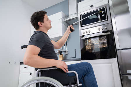 Disabled Man Using Grabber Tool To Control Microwave In Kitchenの写真素材